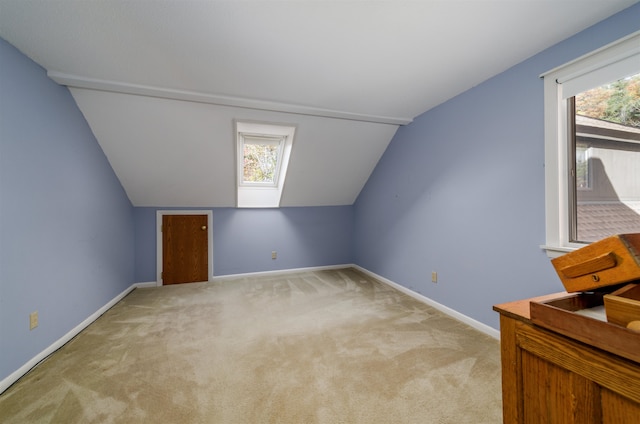 additional living space featuring vaulted ceiling with skylight, light carpet, and plenty of natural light