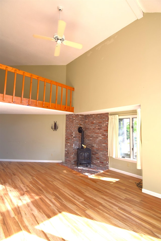 unfurnished living room with hardwood / wood-style floors, ceiling fan, high vaulted ceiling, beamed ceiling, and a wood stove