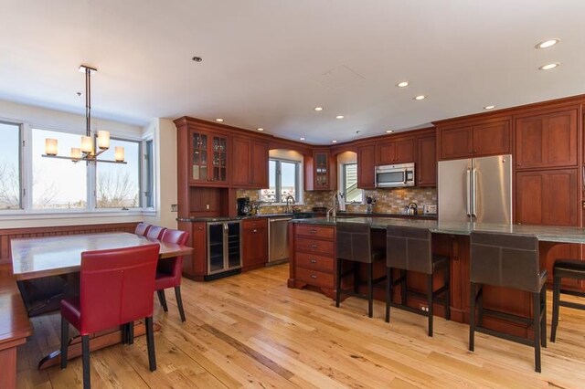 kitchen with wine cooler, decorative light fixtures, appliances with stainless steel finishes, a notable chandelier, and light hardwood / wood-style floors