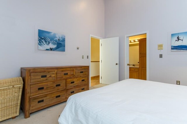 bedroom with connected bathroom, a towering ceiling, and light colored carpet