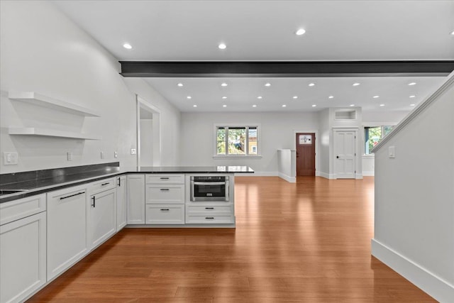 kitchen with open shelves, dark countertops, light wood finished floors, stainless steel oven, and a peninsula