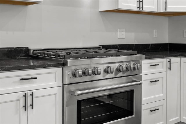 kitchen with dark stone countertops, high end stove, and white cabinetry