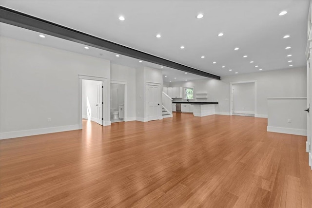 unfurnished living room featuring baseboards, light wood-style flooring, and stairs