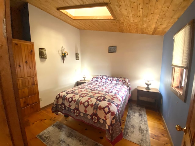 bedroom featuring vaulted ceiling with skylight, light hardwood / wood-style floors, and wood ceiling