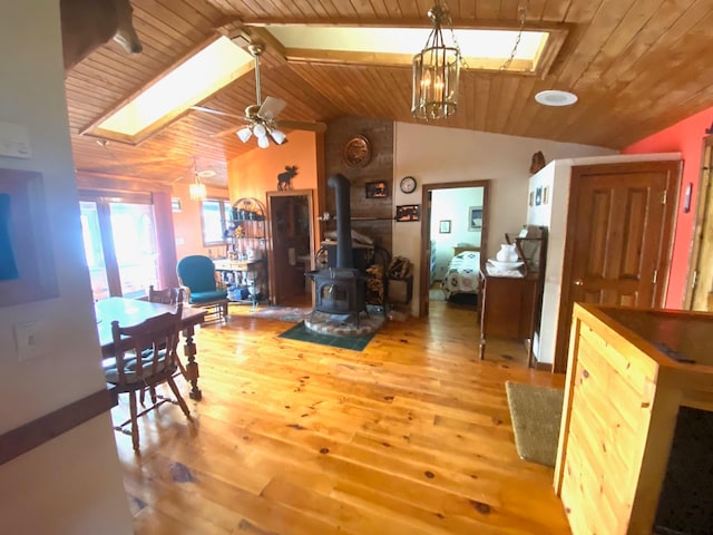 dining area featuring ceiling fan, vaulted ceiling with skylight, a wood stove, light hardwood / wood-style flooring, and wooden ceiling