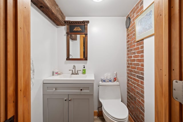 bathroom featuring vanity, toilet, and brick wall