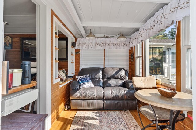 living room with light hardwood / wood-style floors, wood walls, and beamed ceiling