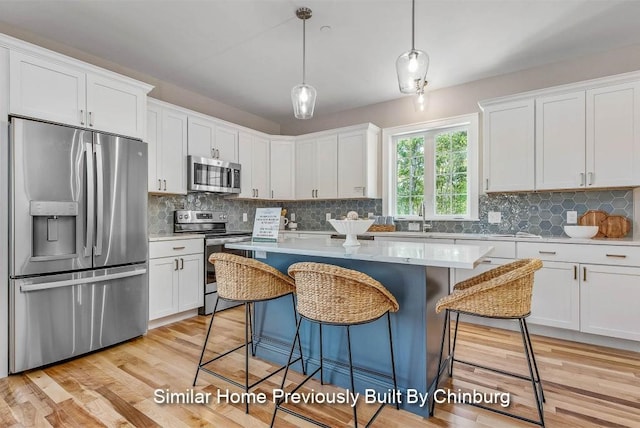 kitchen with light hardwood / wood-style floors, white cabinetry, hanging light fixtures, and appliances with stainless steel finishes