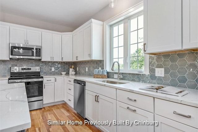 kitchen with sink, stainless steel appliances, light stone counters, white cabinets, and light wood-type flooring