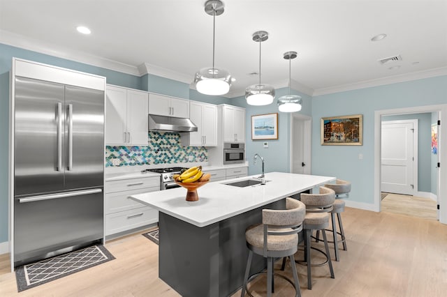 kitchen with hanging light fixtures, white cabinets, premium appliances, a kitchen island with sink, and sink