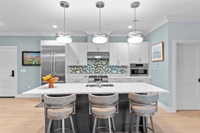 kitchen with a kitchen island with sink, sink, stainless steel appliances, and decorative light fixtures