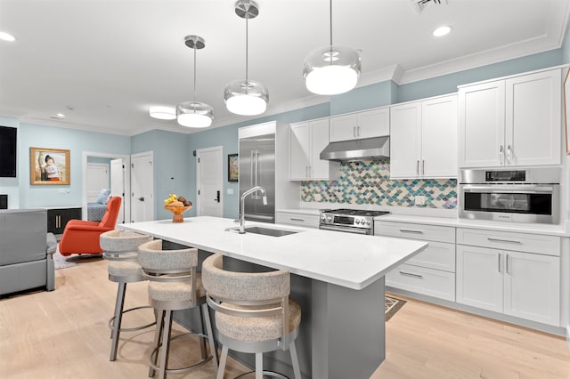 kitchen with light wood-type flooring, sink, white cabinetry, stainless steel appliances, and decorative light fixtures