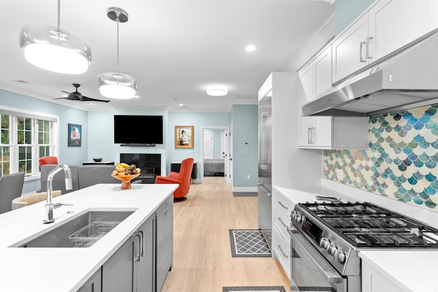 kitchen featuring white cabinets, pendant lighting, stainless steel stove, light wood-type flooring, and sink