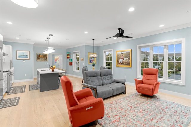 living room with ceiling fan with notable chandelier, ornamental molding, and light hardwood / wood-style flooring