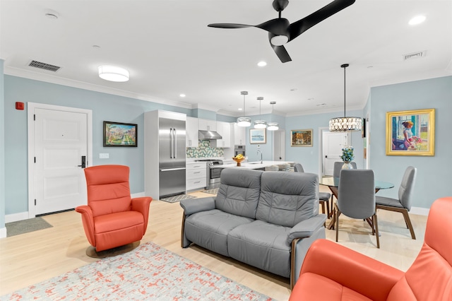 living room featuring ceiling fan with notable chandelier, light wood-type flooring, ornamental molding, and sink