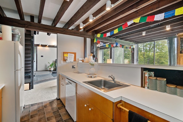 kitchen with beam ceiling, sink, white appliances, track lighting, and dark colored carpet