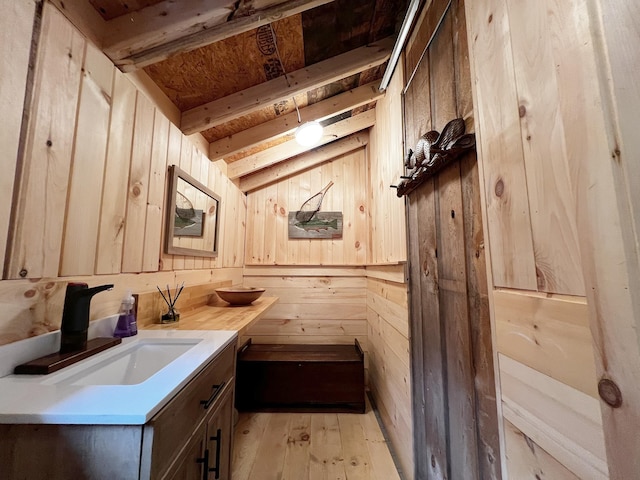 kitchen with light countertops, wooden walls, a sink, light wood-style floors, and vaulted ceiling with beams