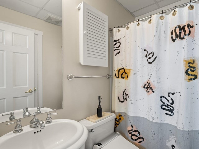 bathroom with a paneled ceiling, toilet, and sink