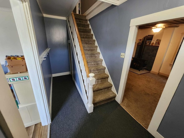 stairs with carpet floors, a wood stove, and baseboards