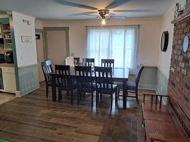 dining space with wainscoting, dark wood-style flooring, a ceiling fan, and ornamental molding