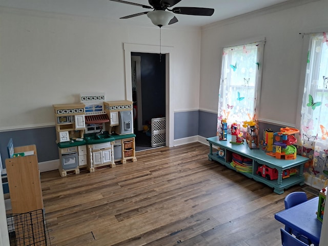 rec room with baseboards, wood finished floors, ornamental molding, and ceiling fan