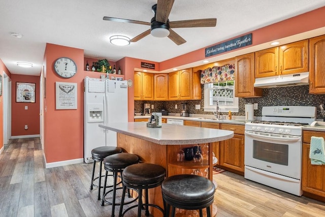 kitchen with a kitchen bar, a kitchen island, light hardwood / wood-style flooring, white appliances, and ceiling fan