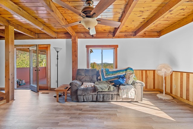 living area with ceiling fan, beamed ceiling, wood walls, wooden ceiling, and light wood-type flooring