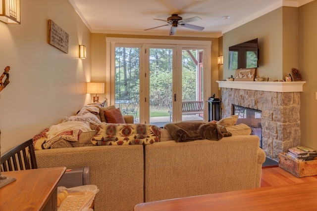 living room featuring ceiling fan, a stone fireplace, crown molding, and hardwood / wood-style floors