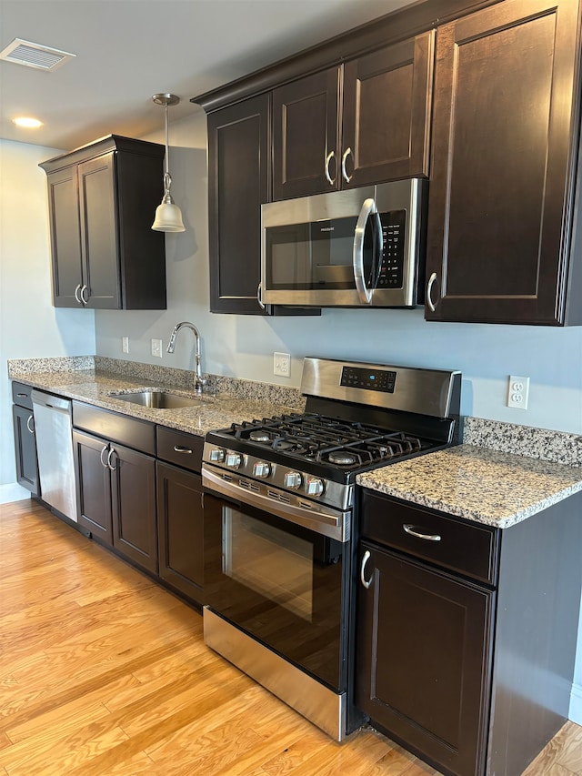 kitchen with light stone countertops, sink, pendant lighting, light hardwood / wood-style floors, and appliances with stainless steel finishes