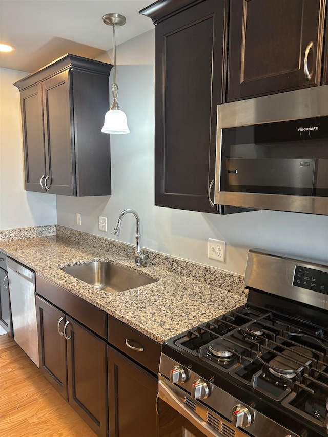 kitchen with sink, light wood-type flooring, light stone counters, dark brown cabinetry, and stainless steel appliances