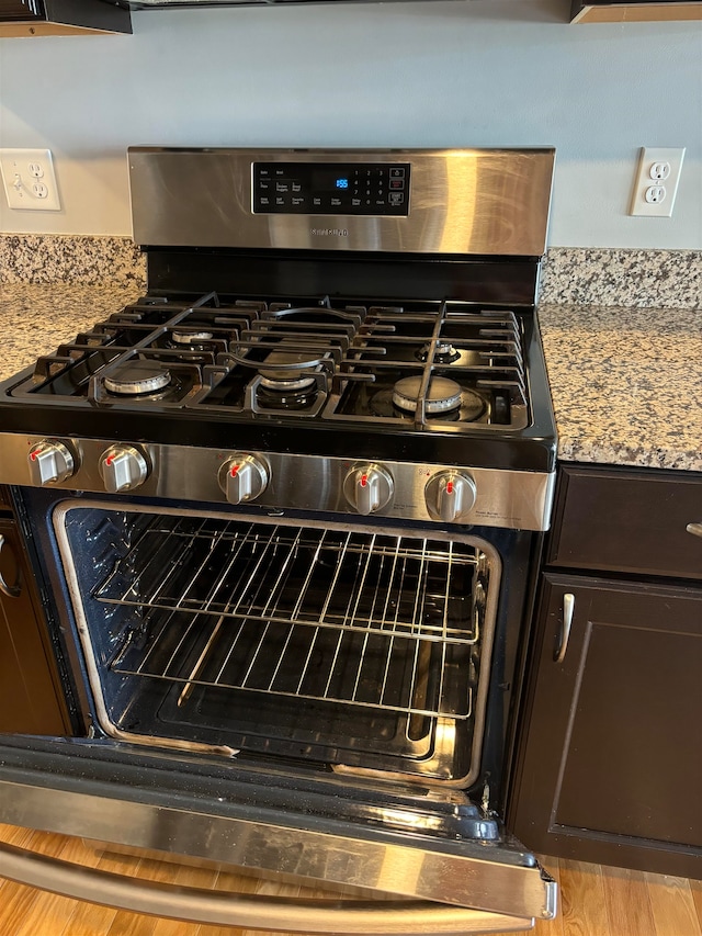 details with gas stove, light stone counters, and dark brown cabinets