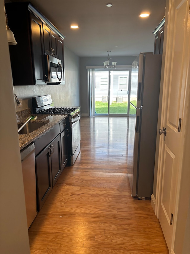 kitchen with dark stone countertops, tasteful backsplash, stainless steel appliances, light hardwood / wood-style flooring, and a notable chandelier