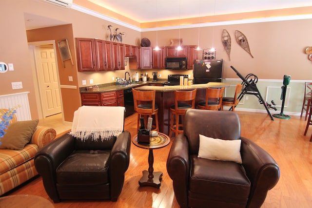 kitchen with light wood-type flooring, sink, hanging light fixtures, a kitchen breakfast bar, and black appliances