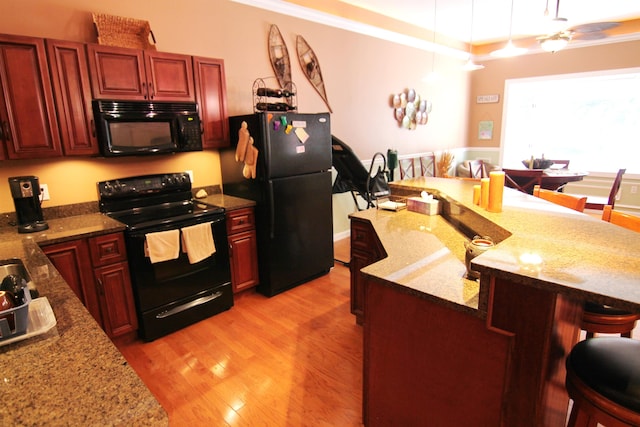 kitchen with a kitchen breakfast bar, hanging light fixtures, light hardwood / wood-style floors, light stone countertops, and black appliances