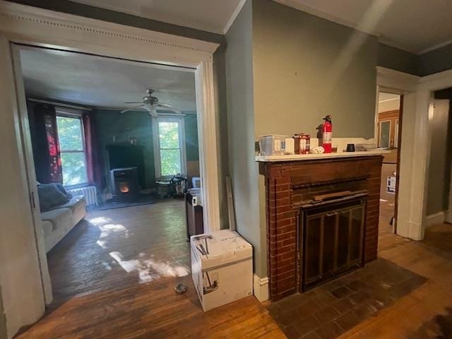 interior space with a brick fireplace, ornamental molding, wood-type flooring, and ceiling fan