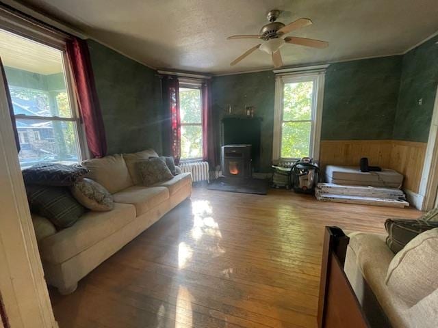 living room featuring wood-type flooring, ceiling fan, a wood stove, and plenty of natural light