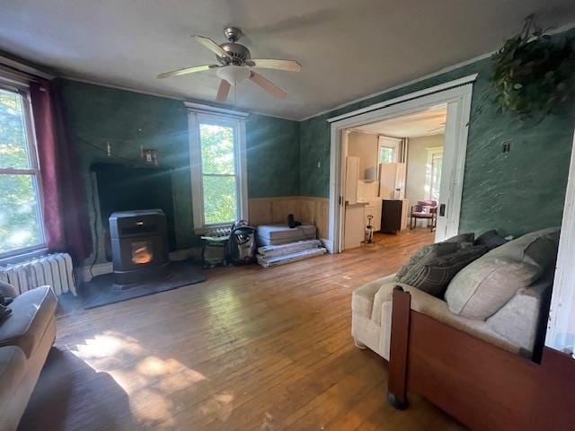 living room featuring radiator heating unit, a wood stove, ceiling fan, and hardwood / wood-style floors