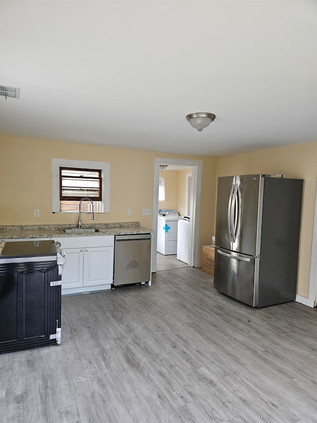 kitchen featuring white cabinetry, stainless steel appliances, light wood-type flooring, sink, and washer and dryer