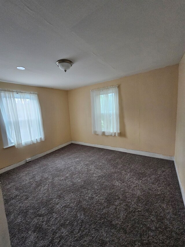 empty room with dark carpet, a textured ceiling, and plenty of natural light