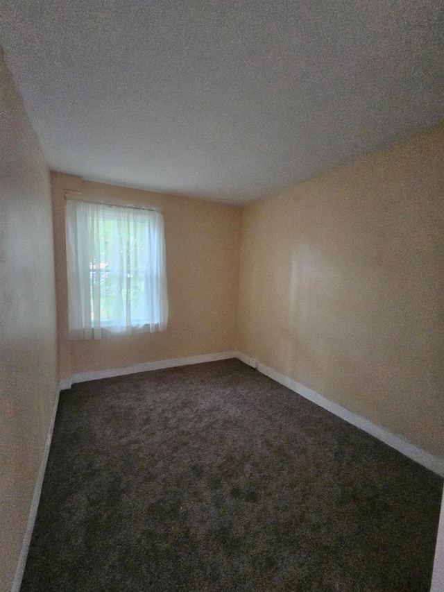 spare room featuring a textured ceiling and dark colored carpet