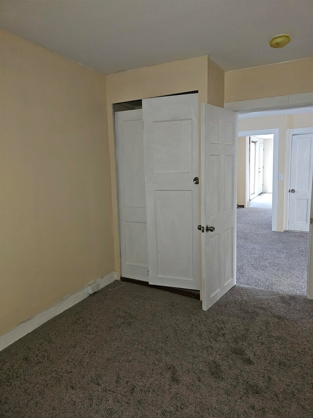 unfurnished bedroom with dark colored carpet and a closet