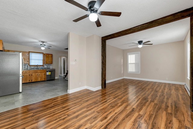 unfurnished living room with dark wood-type flooring, a textured ceiling, beam ceiling, ceiling fan, and sink