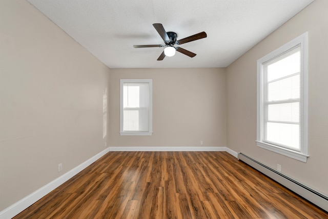 empty room featuring a wealth of natural light, a baseboard heating unit, ceiling fan, and dark hardwood / wood-style floors