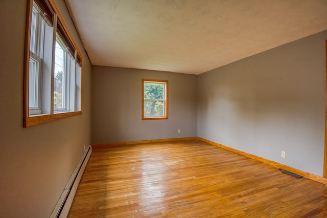 empty room with a baseboard heating unit, light wood-style flooring, a healthy amount of sunlight, and baseboards