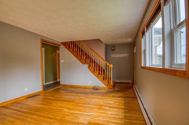 spare room with wood finished floors, stairs, baseboards, and a baseboard radiator