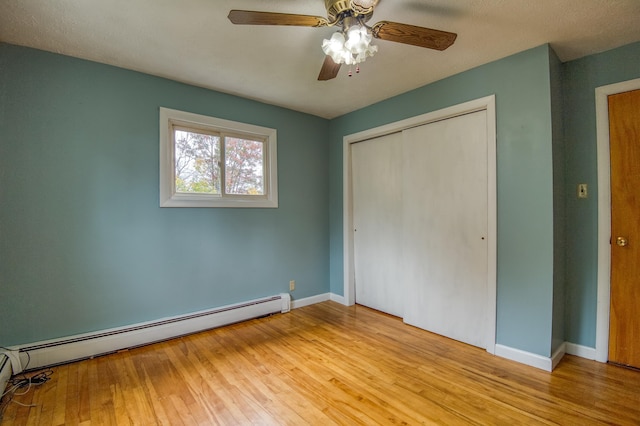 unfurnished bedroom featuring a baseboard heating unit, baseboards, a closet, and wood finished floors