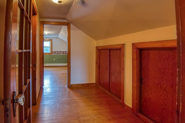 corridor with a baseboard heating unit, lofted ceiling, wood finished floors, and baseboards