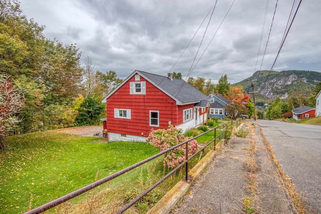 view of property exterior featuring a mountain view, a lawn, driveway, and fence