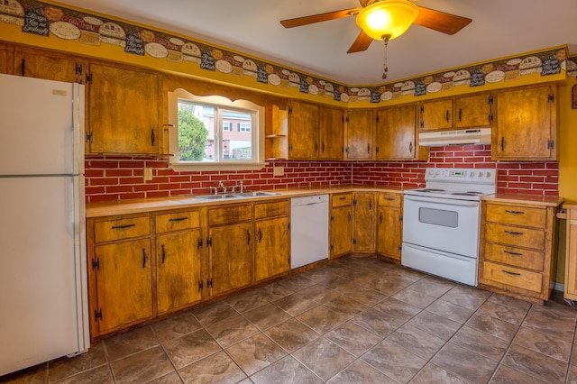 kitchen featuring under cabinet range hood, a sink, backsplash, white appliances, and brown cabinetry