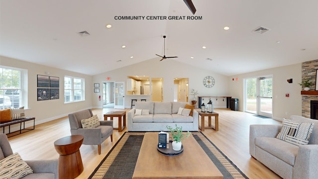 living room featuring light wood-type flooring, a stone fireplace, vaulted ceiling, and ceiling fan